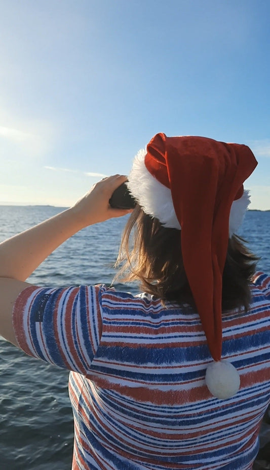 Woman looking in the horizon wearing a Santa hat and nautical shirt