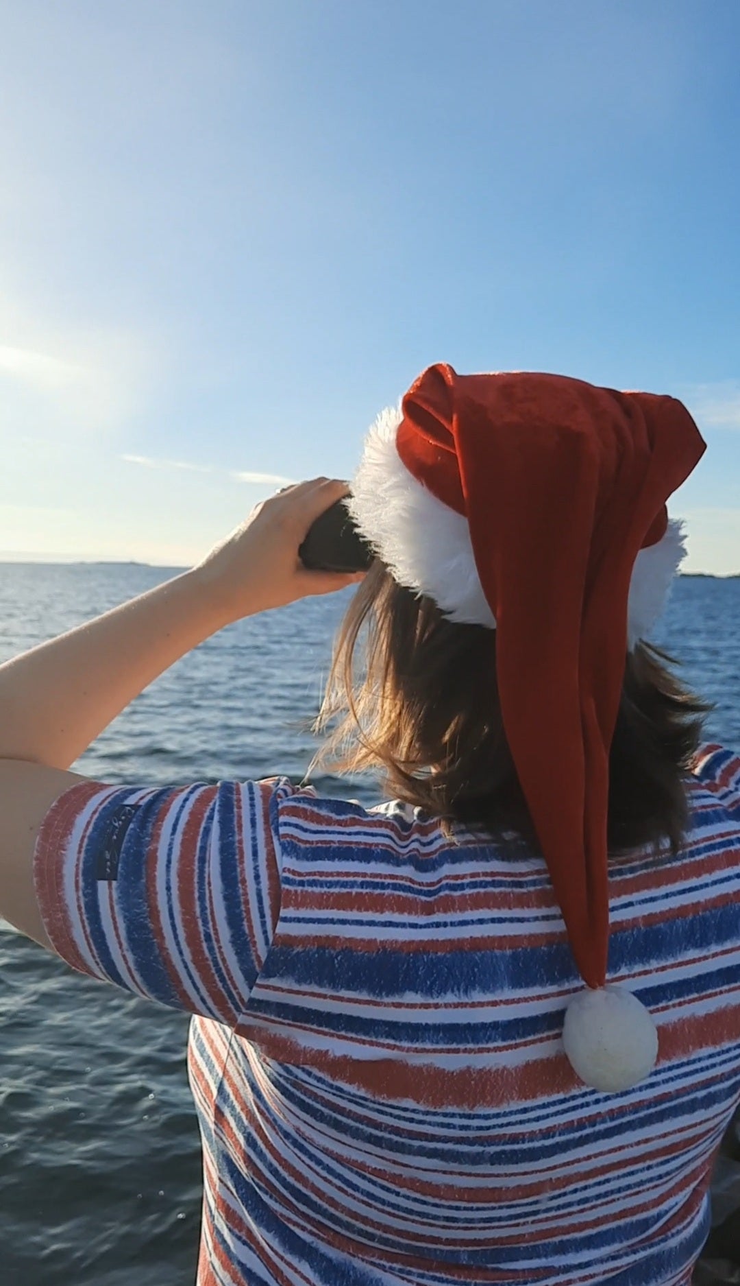 Woman looking in the horizon wearing a Santa hat and nautical shirt