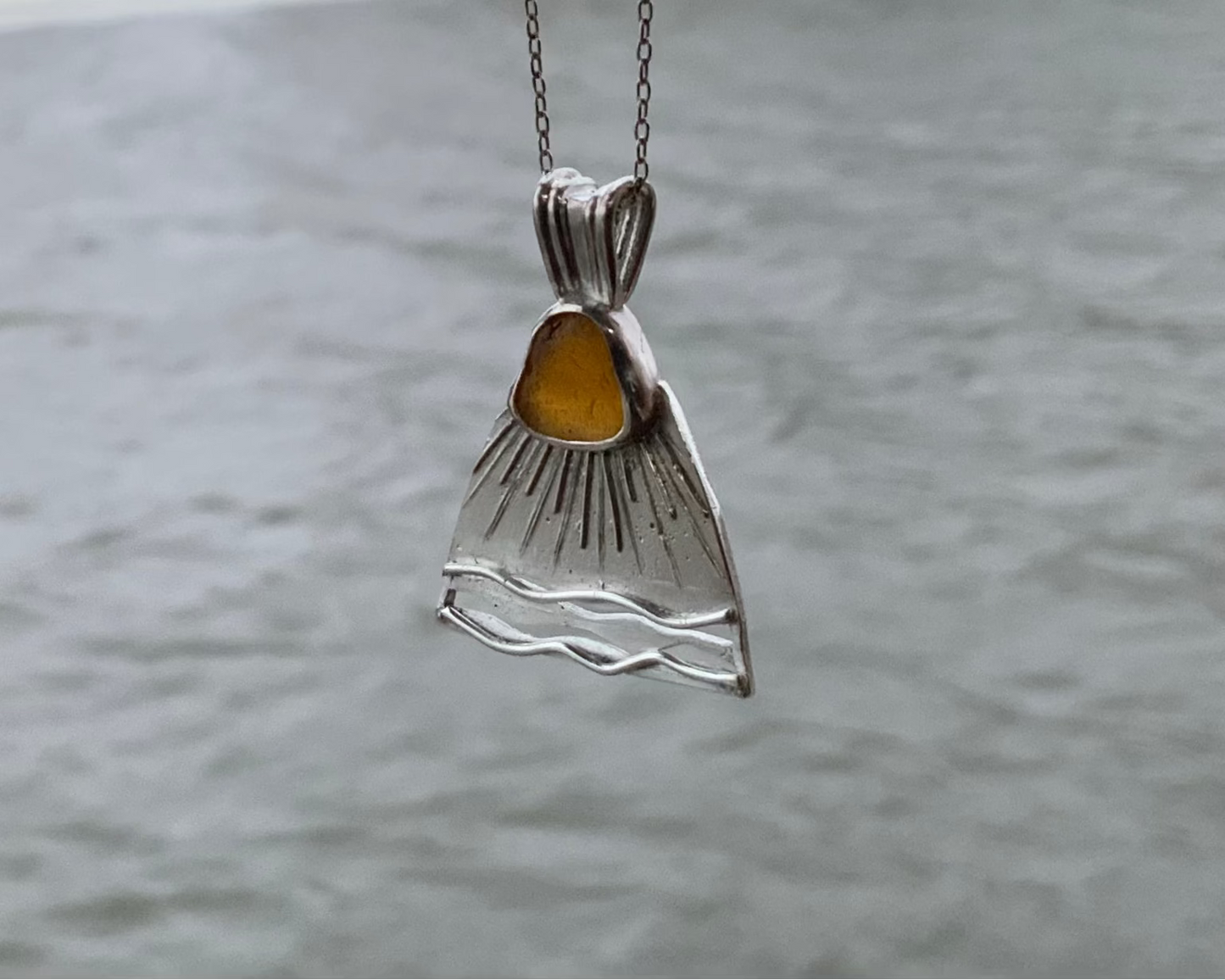 Baltic Sea sun Silver pendant with orange sea glass against a blurred water background