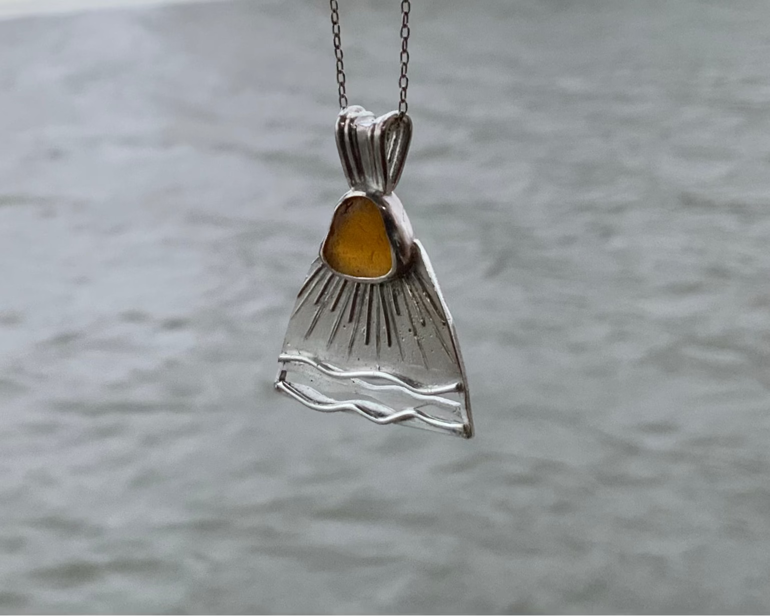 Baltic Sea sun Silver pendant with orange sea glass against a blurred water background