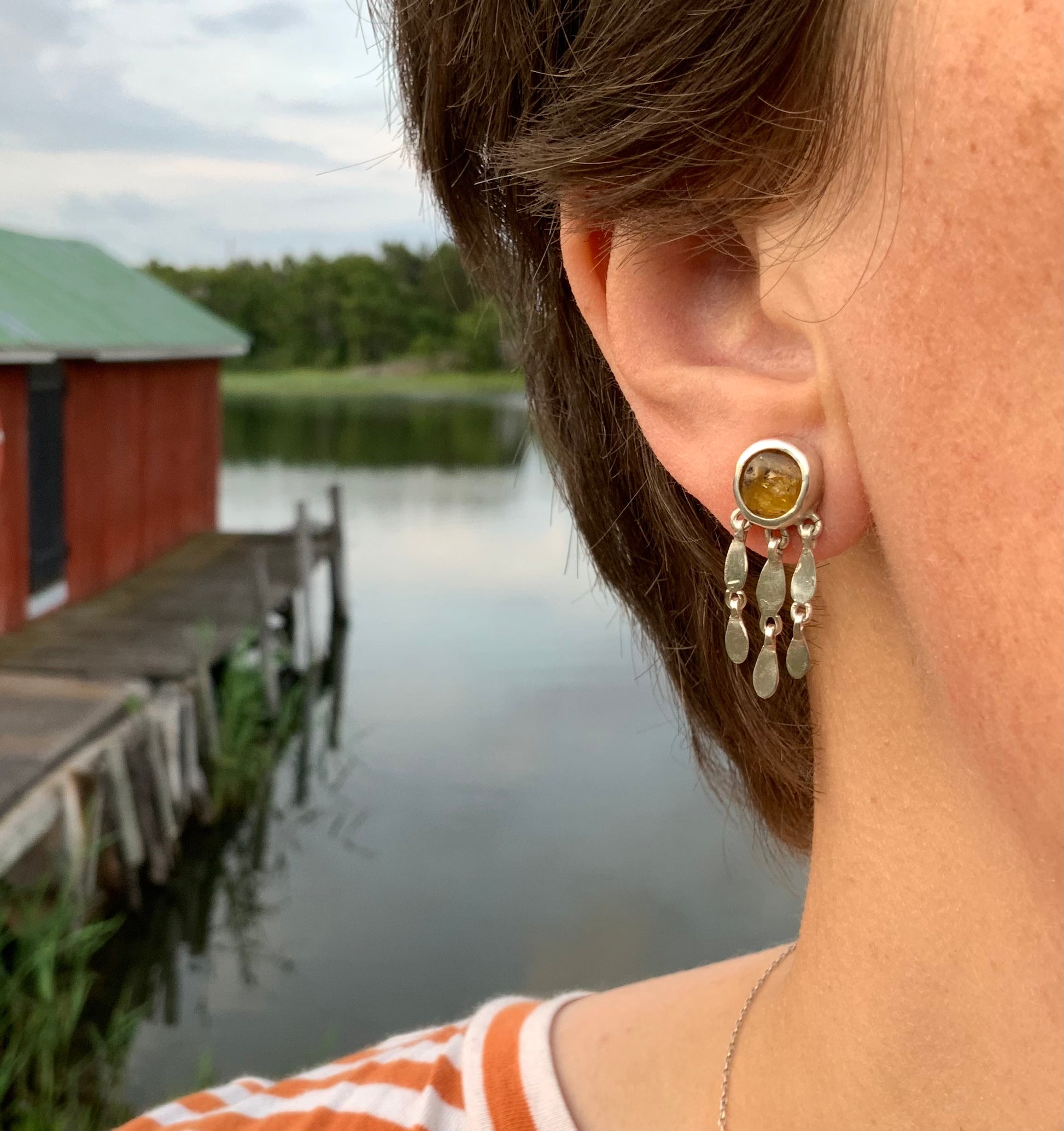 Person wearing earrings with a scenic seaside background and red boathouse