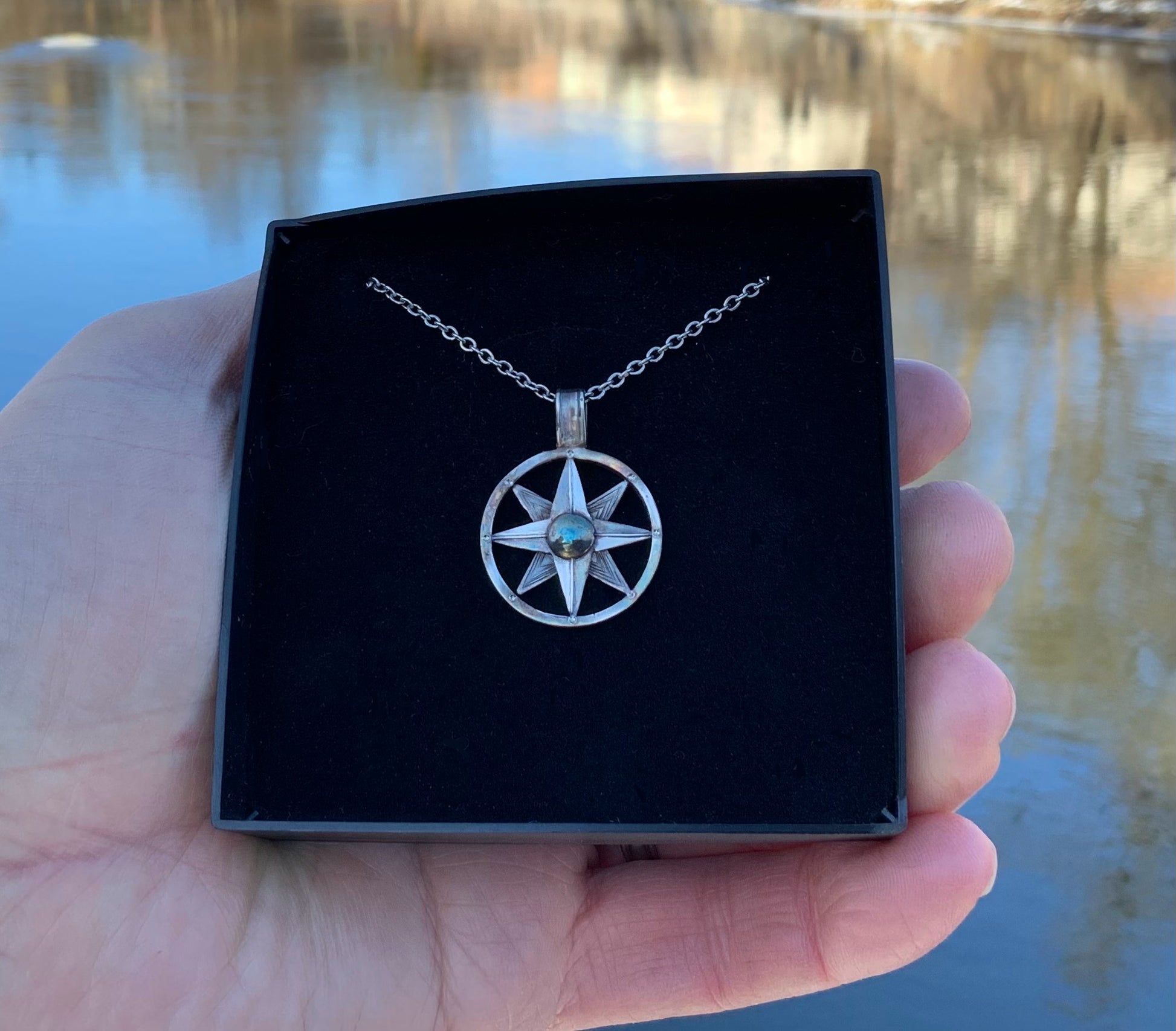 Hand-hammered compass necklace against water