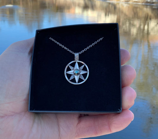 Hand-hammered compass necklace against water