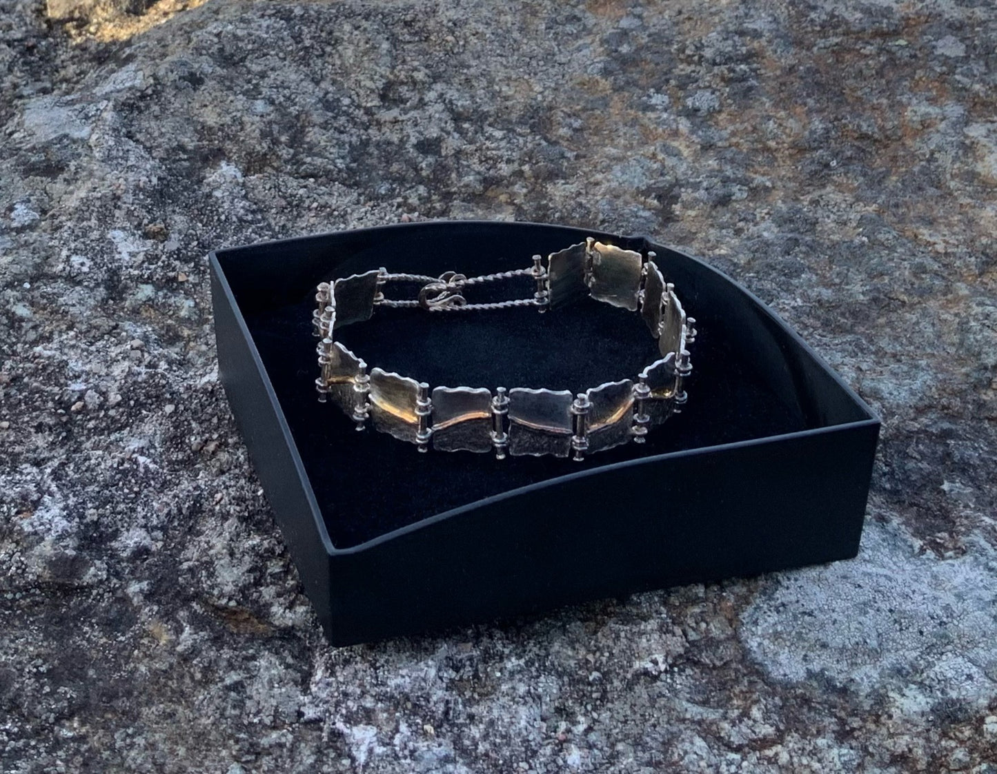 Hand-hammered Silver and gold bracelet in a black box on a stone surface
