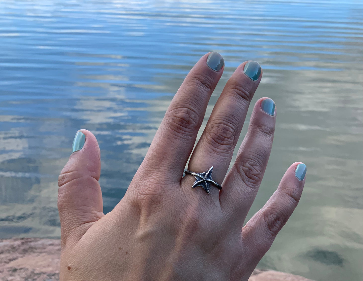 Hand with a silver starfish ring against water