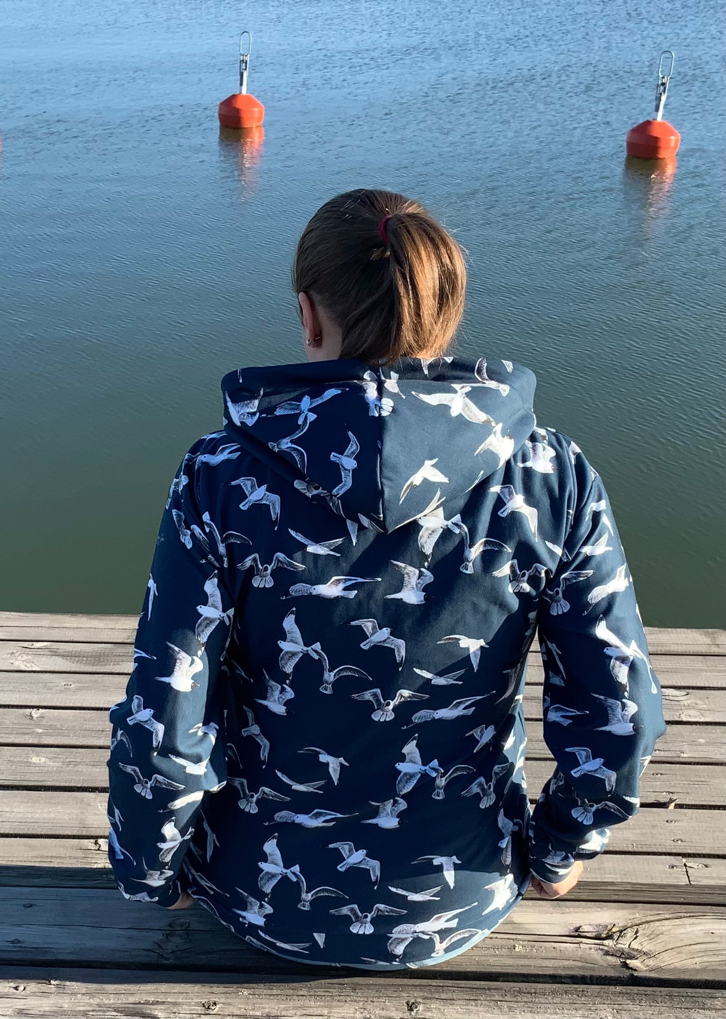 Woman wearing a seagull jacket sitting on a wooden dock by water