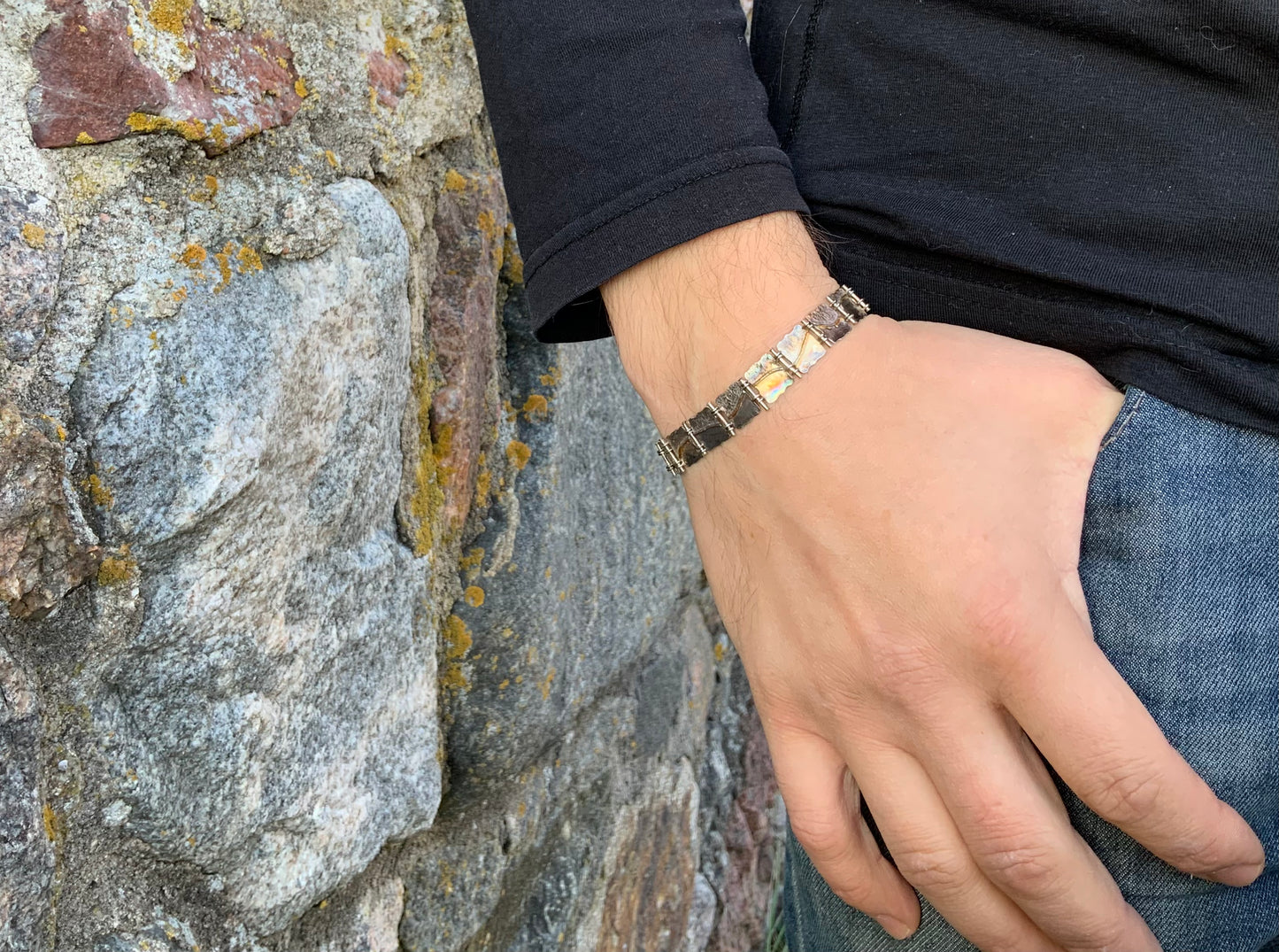 Male hand wearing a geometrical bracelet with a rough stone wall background